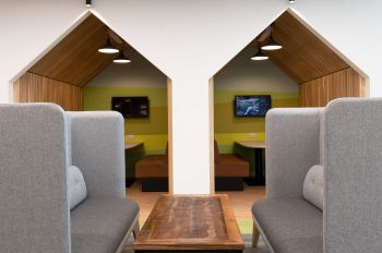 Two grey sofas opposite each other with a low wooden rectangular table between them. In the background, two quiet areas in the shape of beach huts