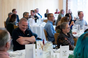 Image of the long service lunch. People sat on tables smiling and talking