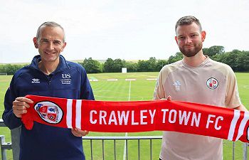 Simon Tunley, Head of Sport at Sussex and Tom Allman, General Manager at Crawley Town FC, pose with a red Crawley Town Football Club scarf with football pitches in the background