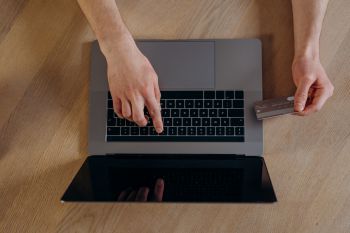 A person's hands using a laptop and holding a credit card