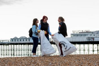 Students participating in a beach clean event with Brighton Pier visible in the background