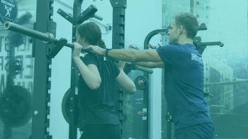 A fitness instructor assisting a woman lifting weights