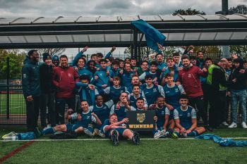 The Sussex men's football team celebrating their win with a varsity winners banner