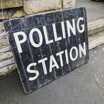 A weathered black sign with the words ‘POLLING STATION’ painted in white capital letters.