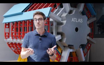 A man standing in front of a large wheel containing an ATLAS logo