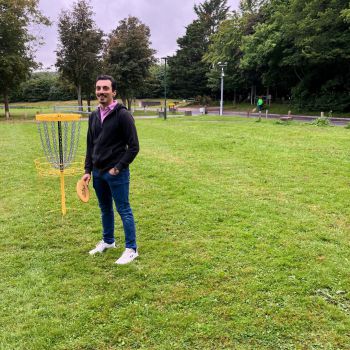 A staff member holding a frisbee next to a frisbee golf basket