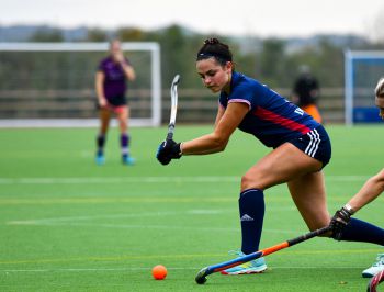 A hockey player raises her stick to hit the ball