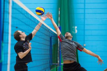 Two men jump for a volleyball at the net.