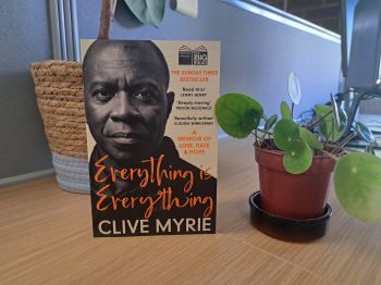 A copy of 'Everything is Everything' by Clive Myrie, propped up next to potted plants