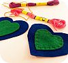 An image of two felt hearts with some pink and red thread that is being used to sew a pattern on them