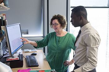 a lecture in green shirt pointing to a computer screen with a student listening and watching the screen