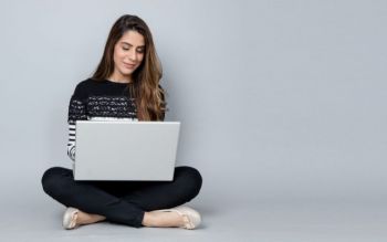 Young woman sitting on the floor against a white wall with a laptop on her lap