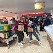 Two students at Eat Central holding a paper bag with food