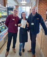 Woman on a black apron holding a certificate flanked by two taller men