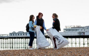 Two students speaking with Kelly Coate near the Palace Pier during a beach clean