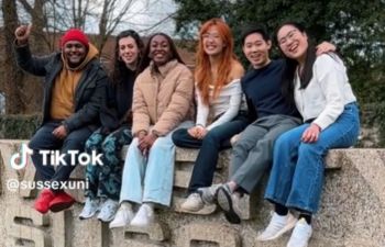 A still from the Digital Media Creator video on TikTok with the new creators sat on the University of Sussex sign