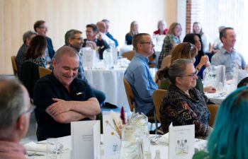 Image of the long service lunch. People sat on tables smiling and talking