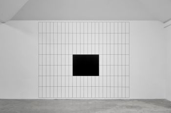 A huge grid drawn on a white wall from floor to ceiling, made from multiple black horizontal and vertical lines with a black square in the centre.