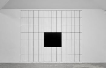 A huge grid drawn on a white wall from floor to ceiling, made from multiple black horizontal and vertical lines with a black square in the centre.