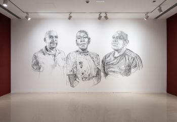 3 large black and white portraits sketched onto a white wall. A black woman centre, 2 black men each side.  Her face is conveying a mix of strength and vulnerability, intricate charcoal strokes create a compelling and emotive portrayal of the subject.