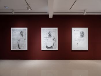 3 black and white charcoal portrait pictures hang on a Burgundy wall. The 2 left portraits are of the same black man, right is of another. Documents of a Job Description and Certificate of Discharge are printed faintly over the subjects.