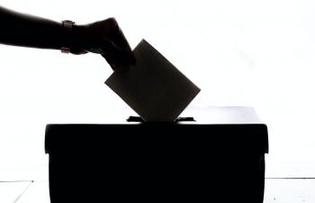 silhouette of a person putting a ballot paper in a ballot box.