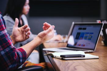 Stock image by Headway. hands gesticulating in front of a laptop screen in the foregroud with a blurred out colleague in the background