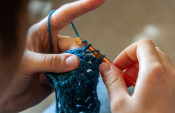 A close up shot of someone crocheting with blue yarn