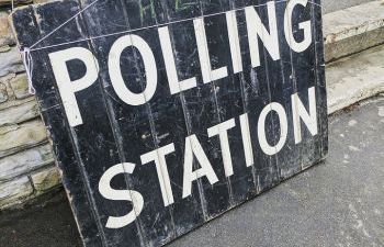 A weathered black sign with the words ‘POLLING STATION’ painted in white capital letters.