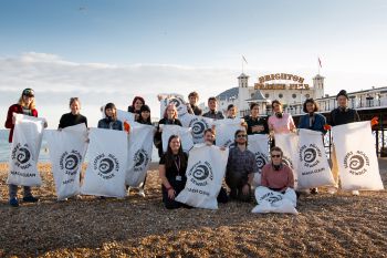 A group of volunteers together on Brighton beach celebrating. They are stood with sacks and gloves after participating in a Brighton beach clean.