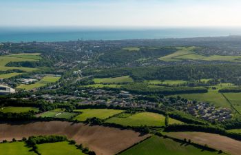 Aerial view of coastal city and green fields under clear skies