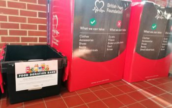 A black Food Bank donation box next to two larger British Heart Foundation donation bins. The British Heart Foundation bins are red with white text detailing what can be donated: clothes, accessories, shoes, books and small electricals.