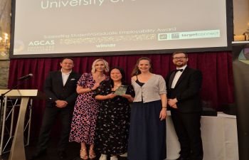 Members of the CEE team stand on stage at the AGCAS awards ceremony, holding a certificate. Behind them is a large screen displaying “University of Sussex Supporting Student/Graduate Employability Award AGCAS winner”