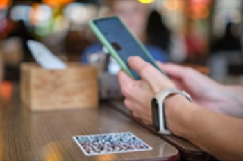 A person holding a smartphone and scanning a QR code which is on the table