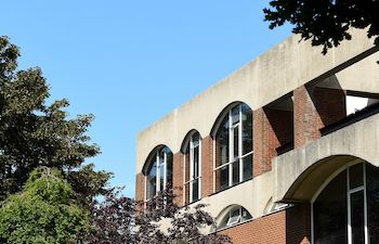 A photograph of a corner of Falmer House at the University of Sussex with trees in the foreground and blue sky above