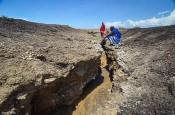 2 Masai men investigating cracked dried Earth in Eastern African lands