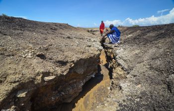 2 Masai men investigating cracked dried Earth in Eastern African lands