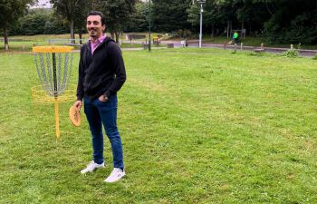 A staff member holding a frisbee next to a frisbee golf basket