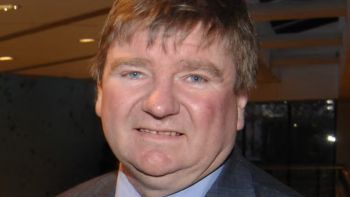 A photo of Professor Trevor Burnard, smiling at the camera. He has brown hair and blue eyes, and is wearing a blue shirt and suit.