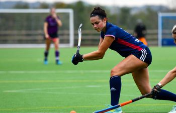 A hockey player raises her stick to hit the ball