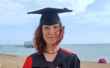 Criminology graduate Lou Bruce wearing graduation gown by Brighton beach