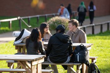 Four students sitting around a picnic bench near Library Square