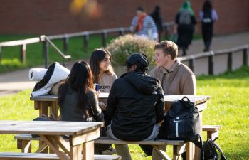 Four students sitting around a picnic bench near Library Square