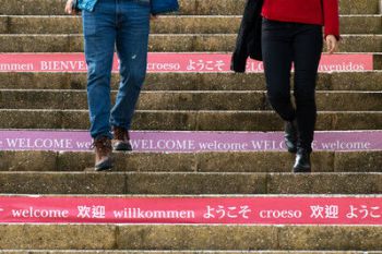 Two people walk down steps with welcome messages in multiple languages on the risers