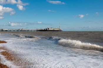 Waves roll in on the shore of Brighton beach with Brighton Pier in the background