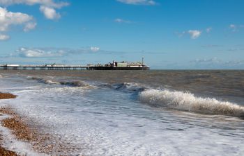 Waves roll in on the shore of Brighton beach with Brighton Pier in the background