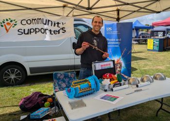 A man standing in front of a table of physics objects on a sunny field