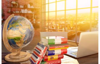 Globe and laptop next to a stack of dictionaries