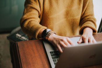 A person wearing a yellow jumper working on a laptop