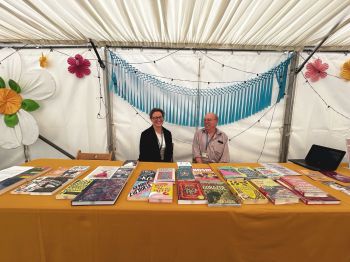 Two members of Library staff smiling and sitting at a table with books on it.